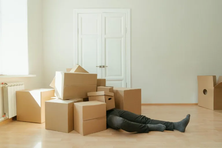 person lying under a pile of empty cardboard boxes. Illustration for blog post: steps to a successful move